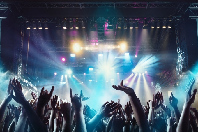 Crowd cheering in front of a music festival stage with a light show.